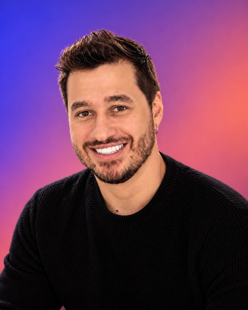 Portrait of Eduardo Gouvêa smiling, wearing a black sweater against a purple-to-coral gradient background